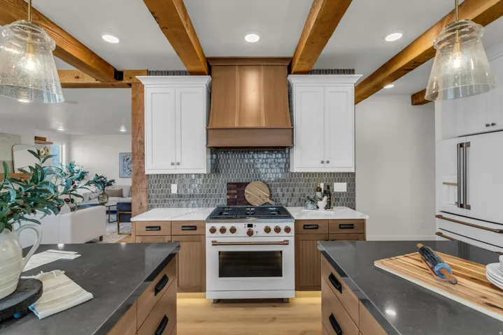 Kitchen featuring exposed wood beams, dual-tone cabinetry, a tiled backsplash, a built-in range, and dark-toned countertops