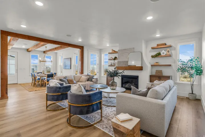 Open-concept living area with wood-finish flooring, exposed ceiling beams, a built-in fireplace, recessed lighting, and multiple windows