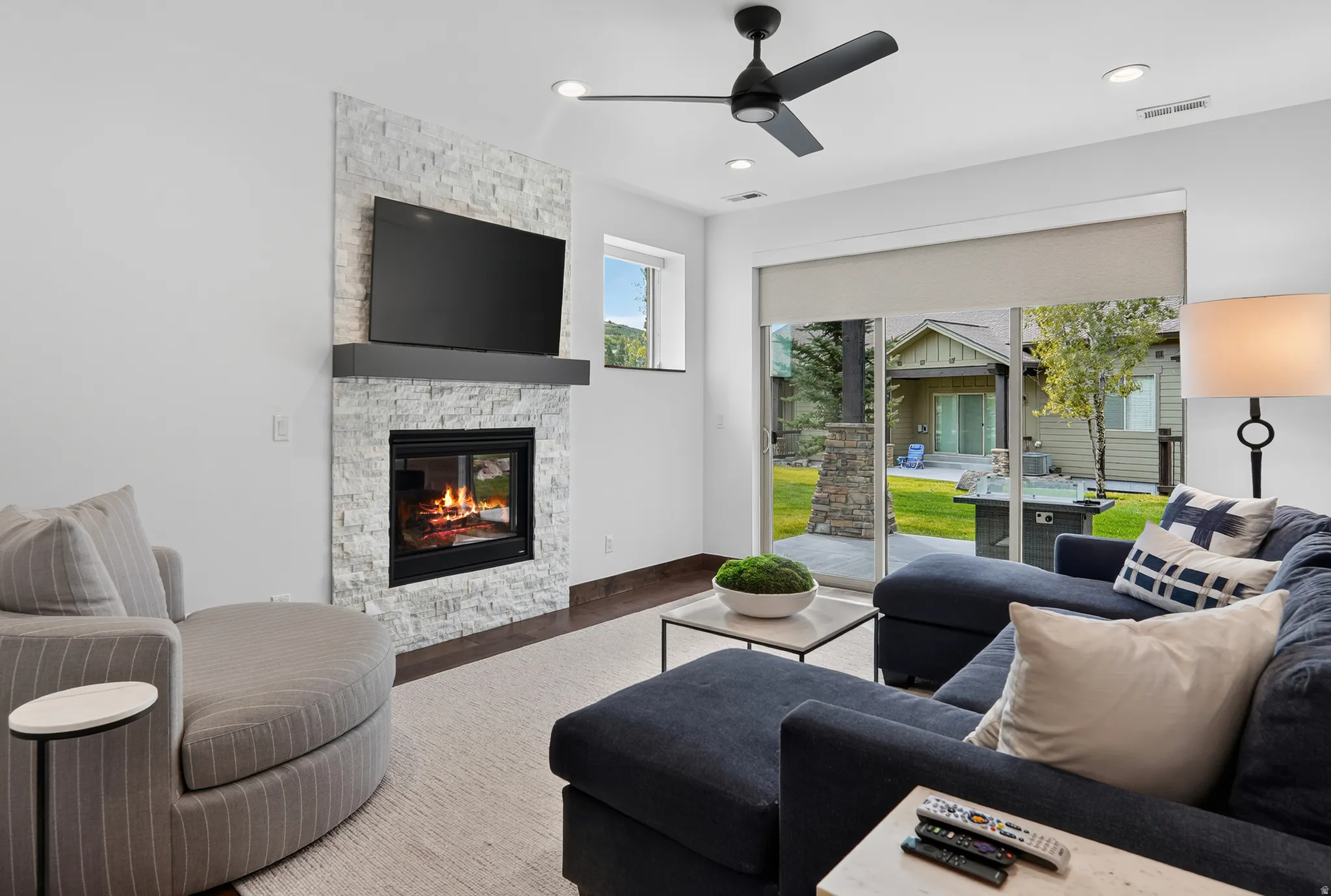 Modern fireplace with stacked stone surround and black mantel, recessed lighting, ceiling fan, and sliding glass door