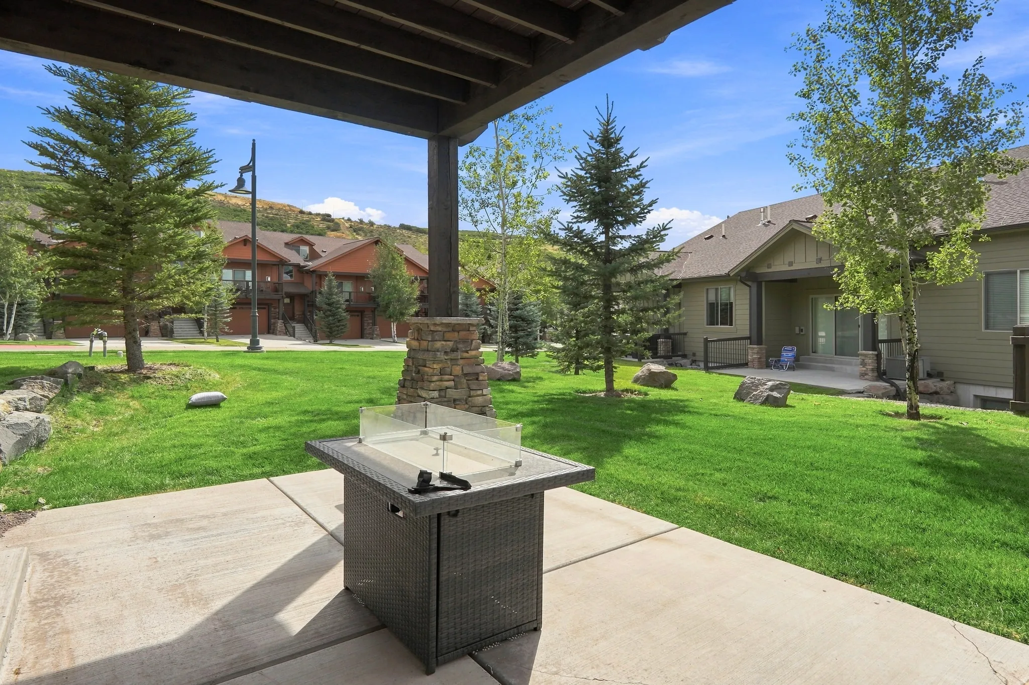 Covered patio with concrete surface, stone pillar, and manicured green lawn