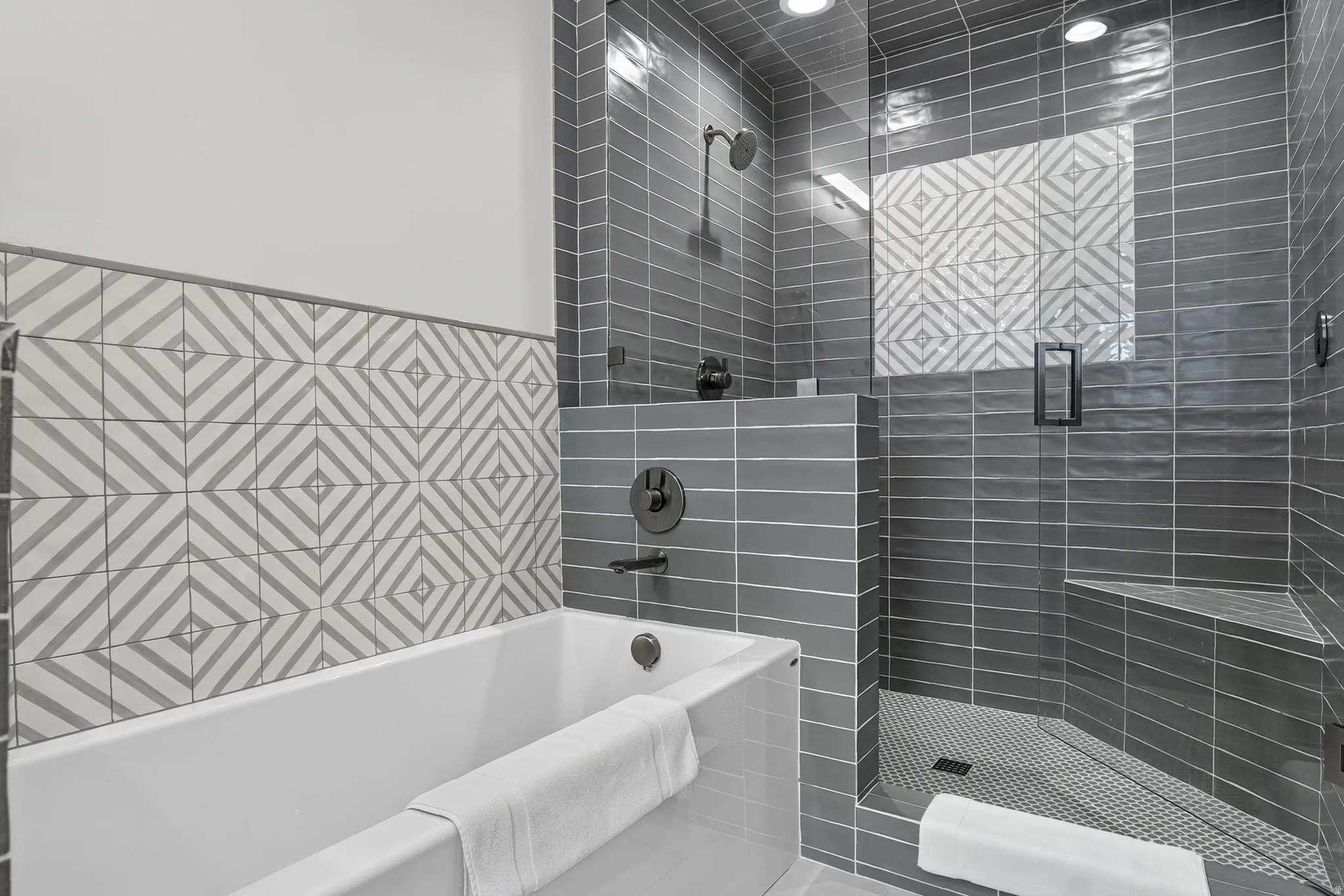 Full-size bathtub, glass-enclosed shower with bench seating, subway tile surround, patterned accent tile, and matte black fixtures