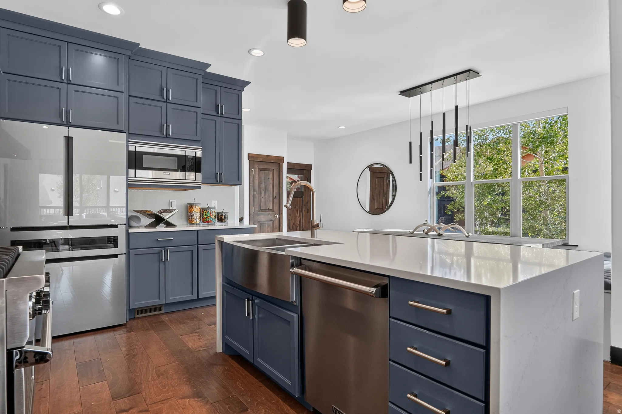 Kitchen featuring blue cabinetry, stainless steel appliances, wood-finish flooring, a kitchen island with a built-in sink, and a multi-light pendant fixture