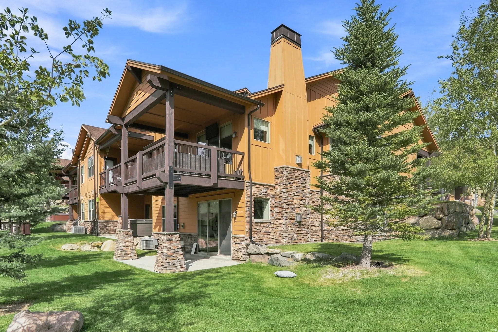Exterior siding with stone accents, a private balcony, a ground-level patio, and extensive landscaping