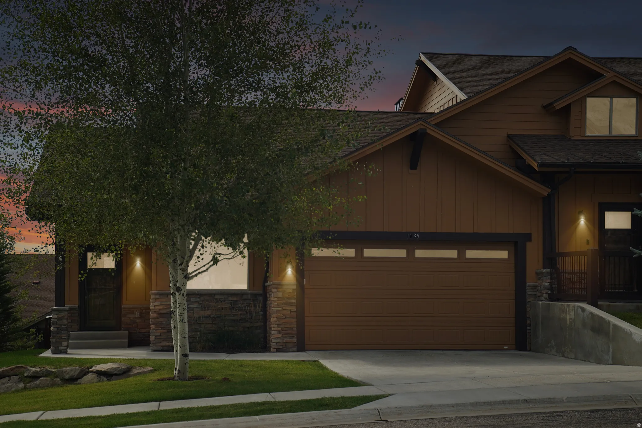 Brown siding exterior with stone accents, a two-car garage, and a covered entry