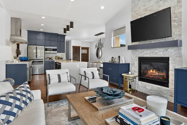 Open-concept living space featuring wood-finish flooring, a stone-clad fireplace, and a recessed entertainment area with a mounted flat-screen