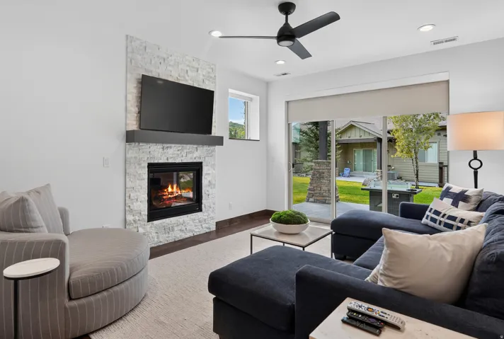 Modern fireplace with stacked stone surround and black mantel, recessed lighting, ceiling fan, and sliding glass door
