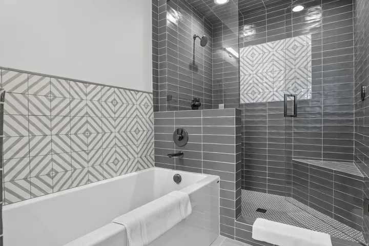 Full-size bathtub, glass-enclosed shower with bench seating, subway tile surround, patterned accent tile, and matte black fixtures