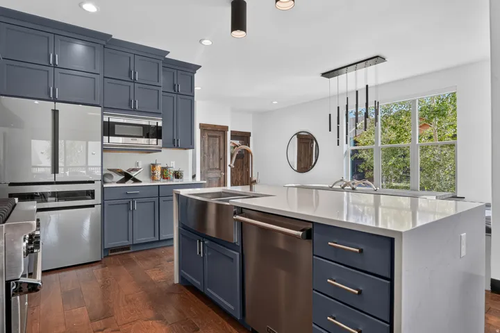 Kitchen featuring blue cabinetry, stainless steel appliances, wood-finish flooring, a kitchen island with a built-in sink, and a multi-light pendant fixture