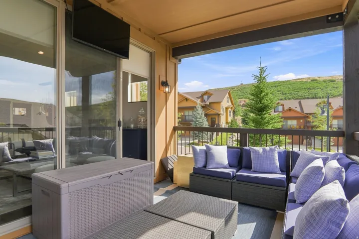 Covered outdoor living area featuring a wood-finish ceiling, sliding glass door access, exterior wall sconces, and a dark wood railing