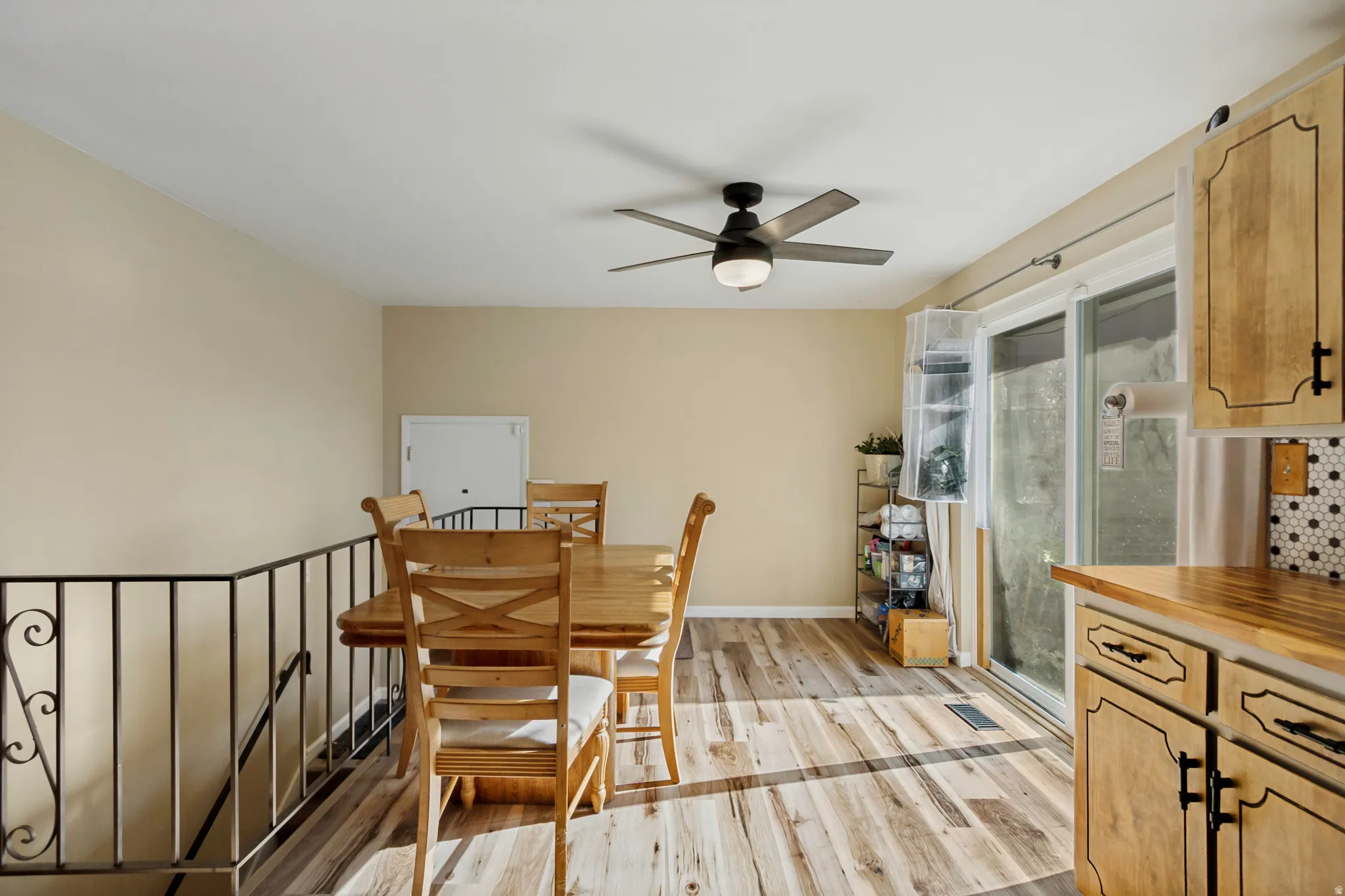 Wood-finish flooring, ceiling fan with integrated lighting, sliding glass door, and a built-in kitchen cabinet