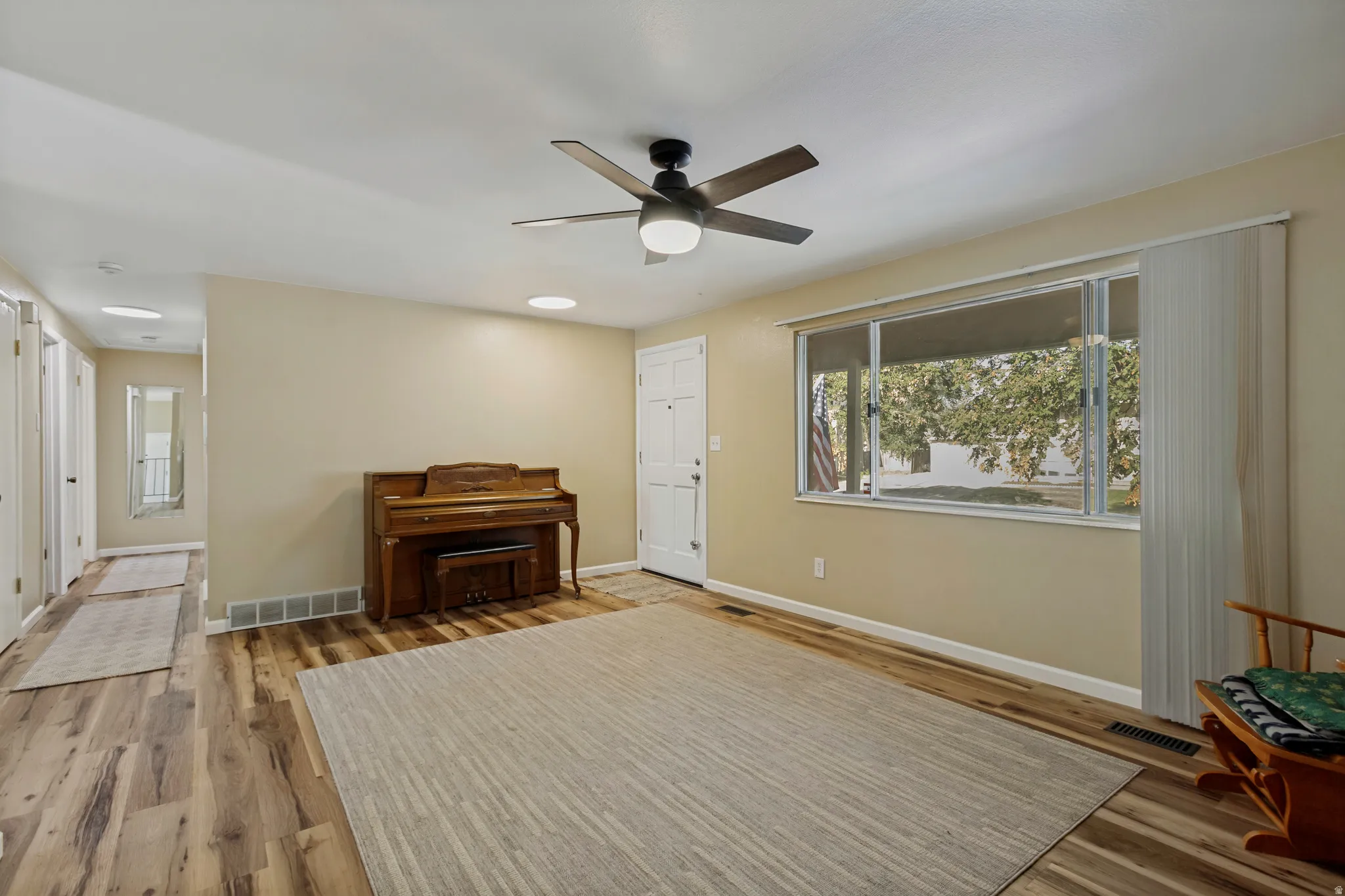 Wood-finish flooring, ceiling fan with integrated lighting, large window with vertical blinds, and neutral painted walls
