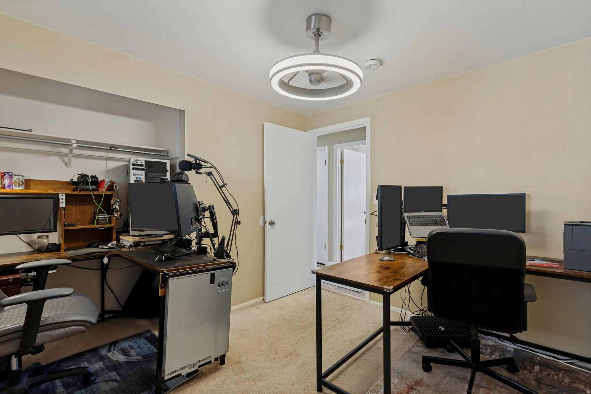 Neutral-toned wall finish, recessed shelving with hanging rods, wood-finish desktop, and a modern ceiling fan with integrated lighting