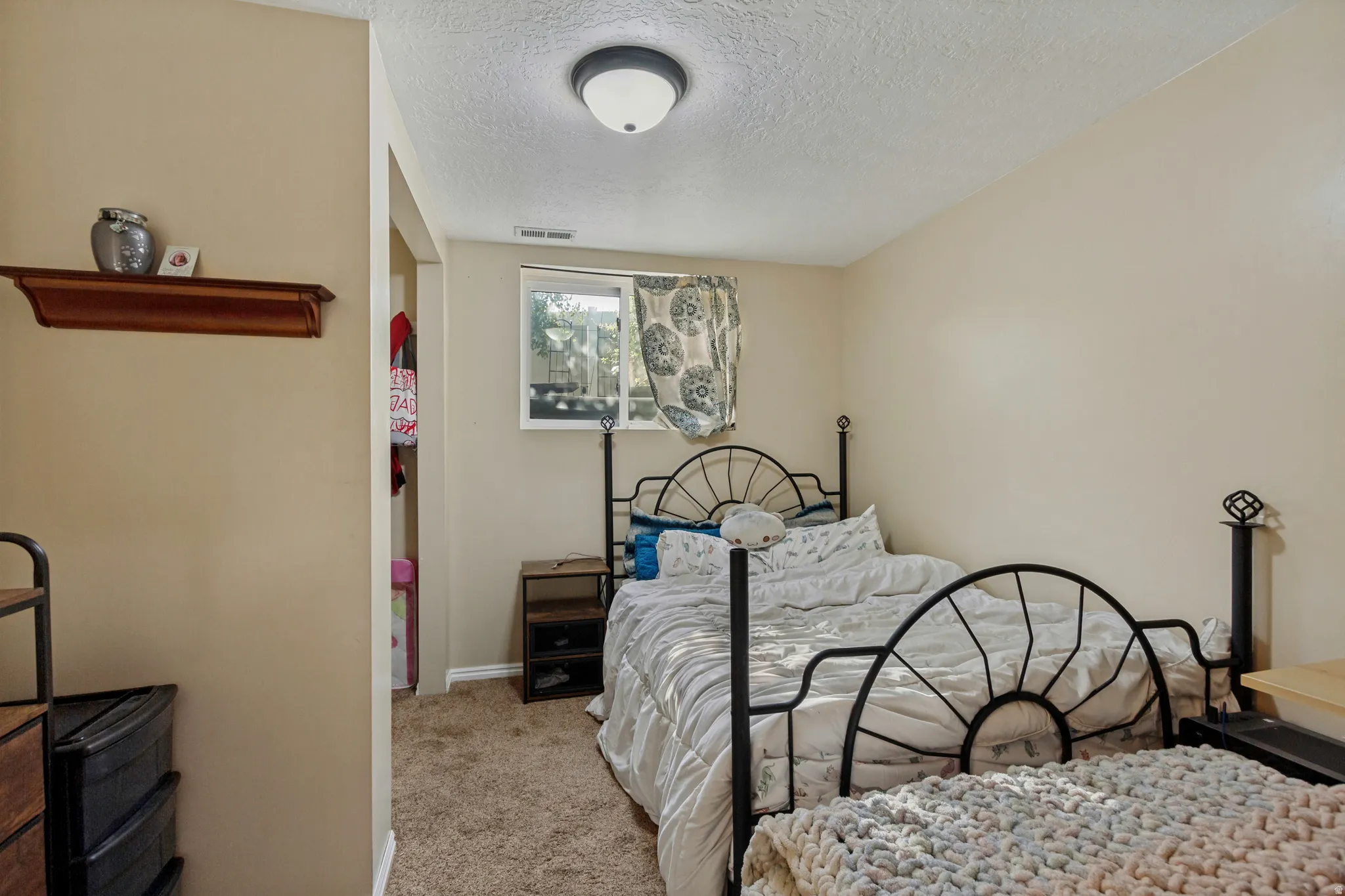 Textured carpet flooring, window with white trim, built-in shelving, and flush-mount ceiling light