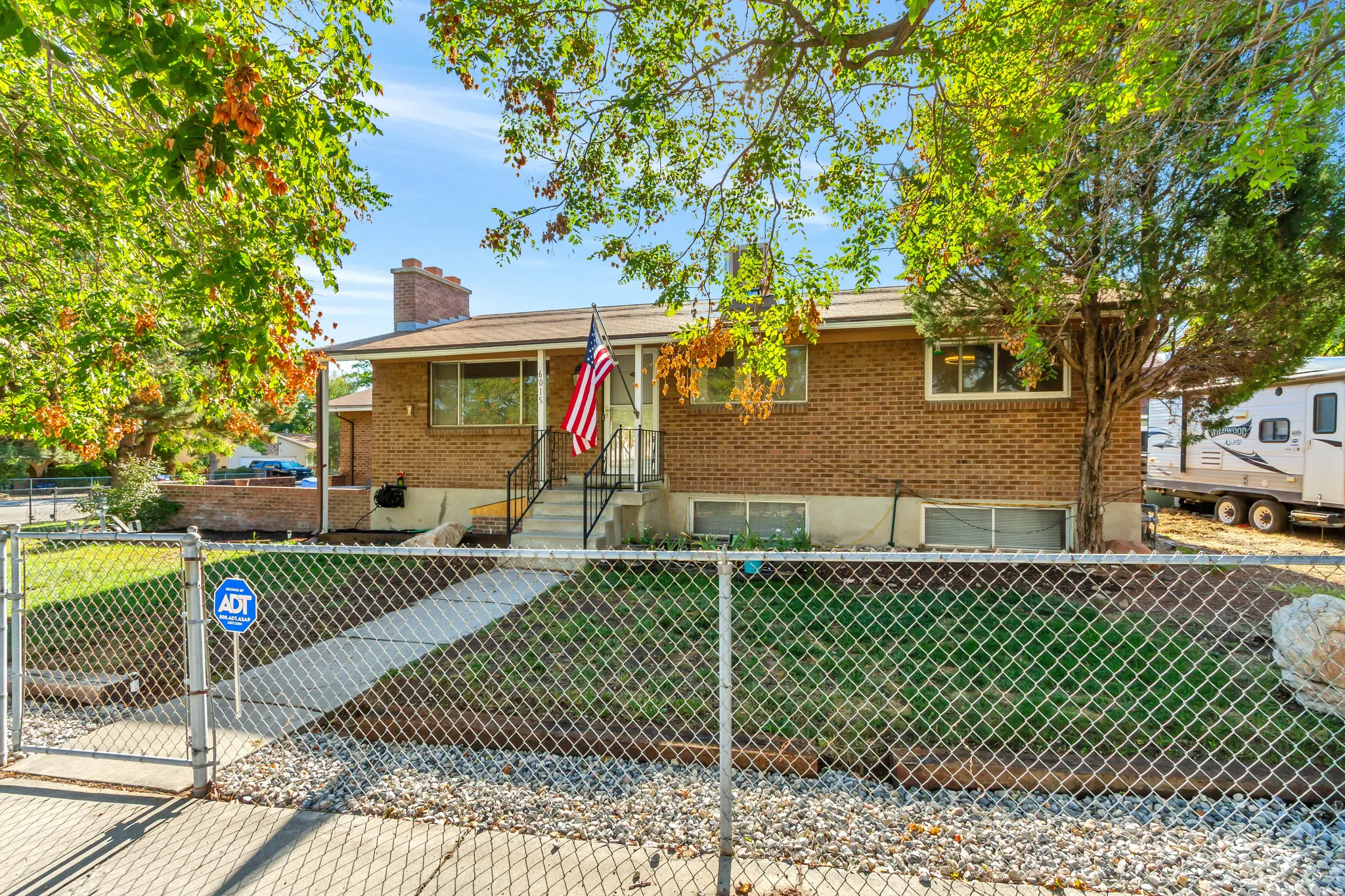 Brick exterior featuring a covered porch with railings, a concrete walkway, and a chain-link fence