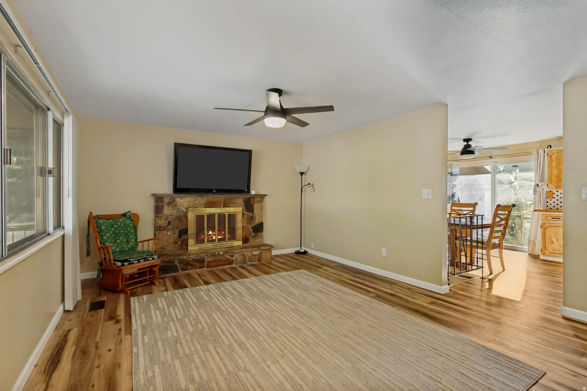Living area featuring a stone-clad fireplace, wood-finish flooring, and a ceiling fan