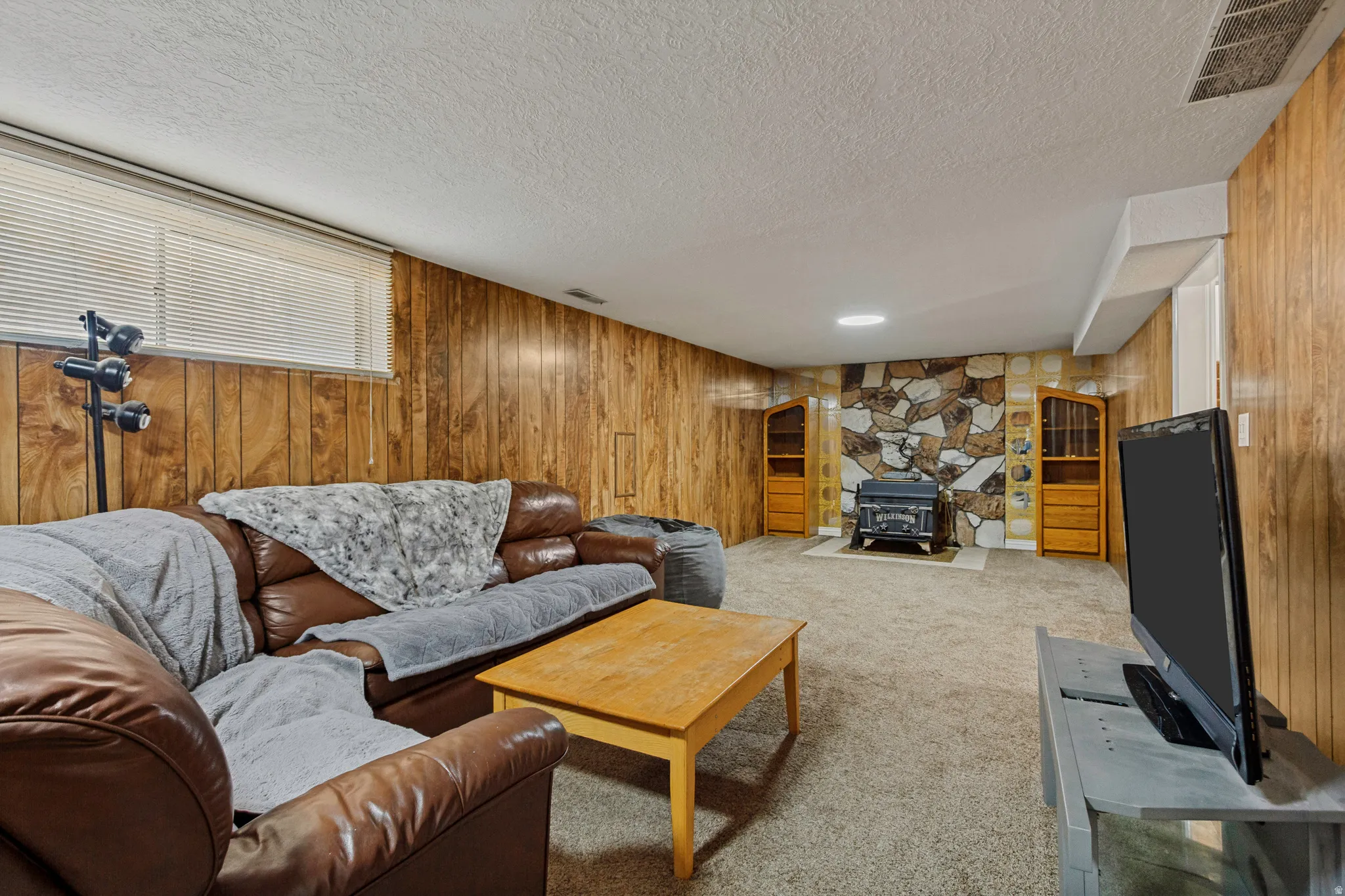 Wood paneling, stone accent wall, recessed lighting, carpet flooring, and a wood-burning stove