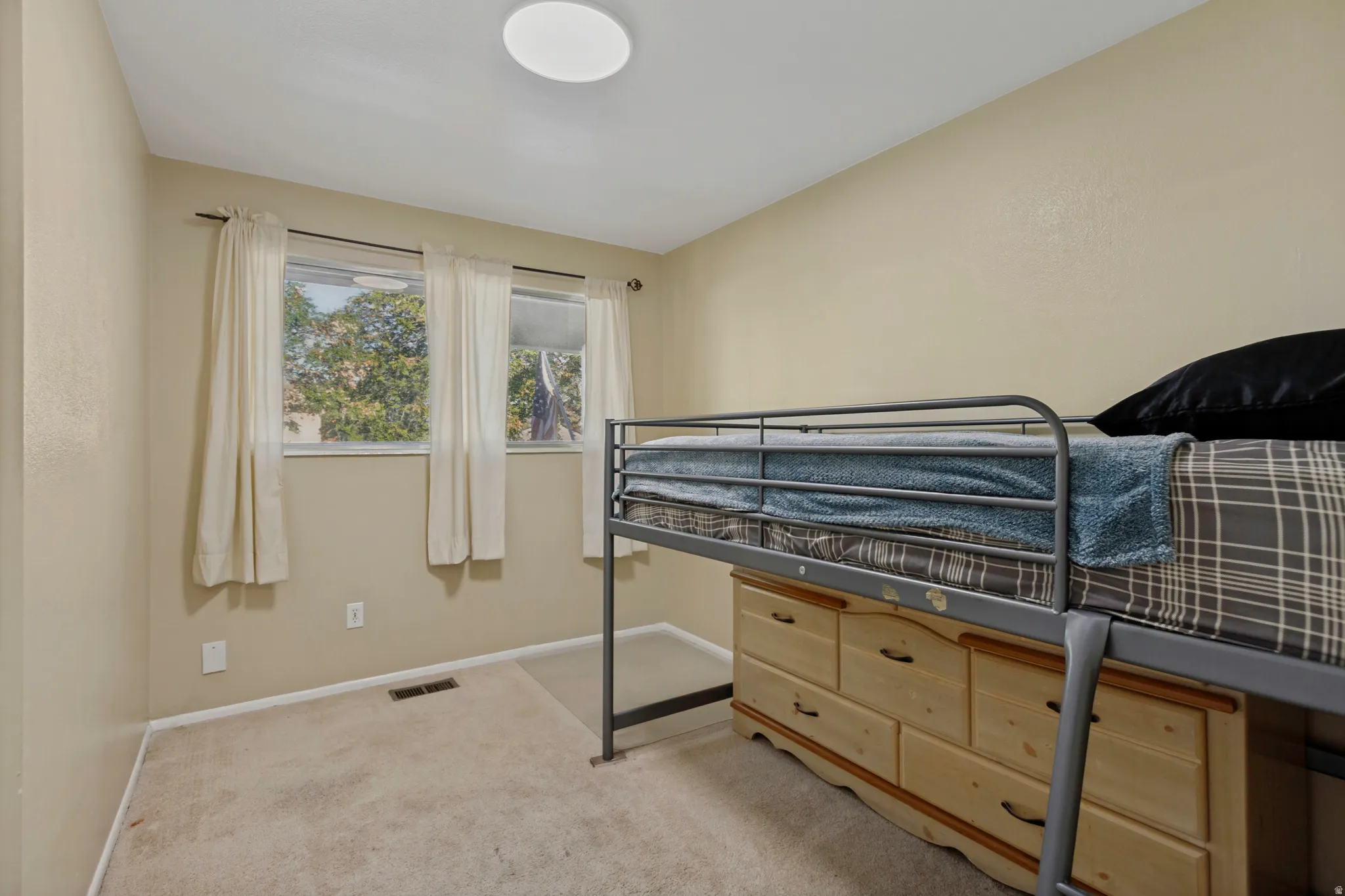 Wall-to-wall carpeting and three windows with white curtains