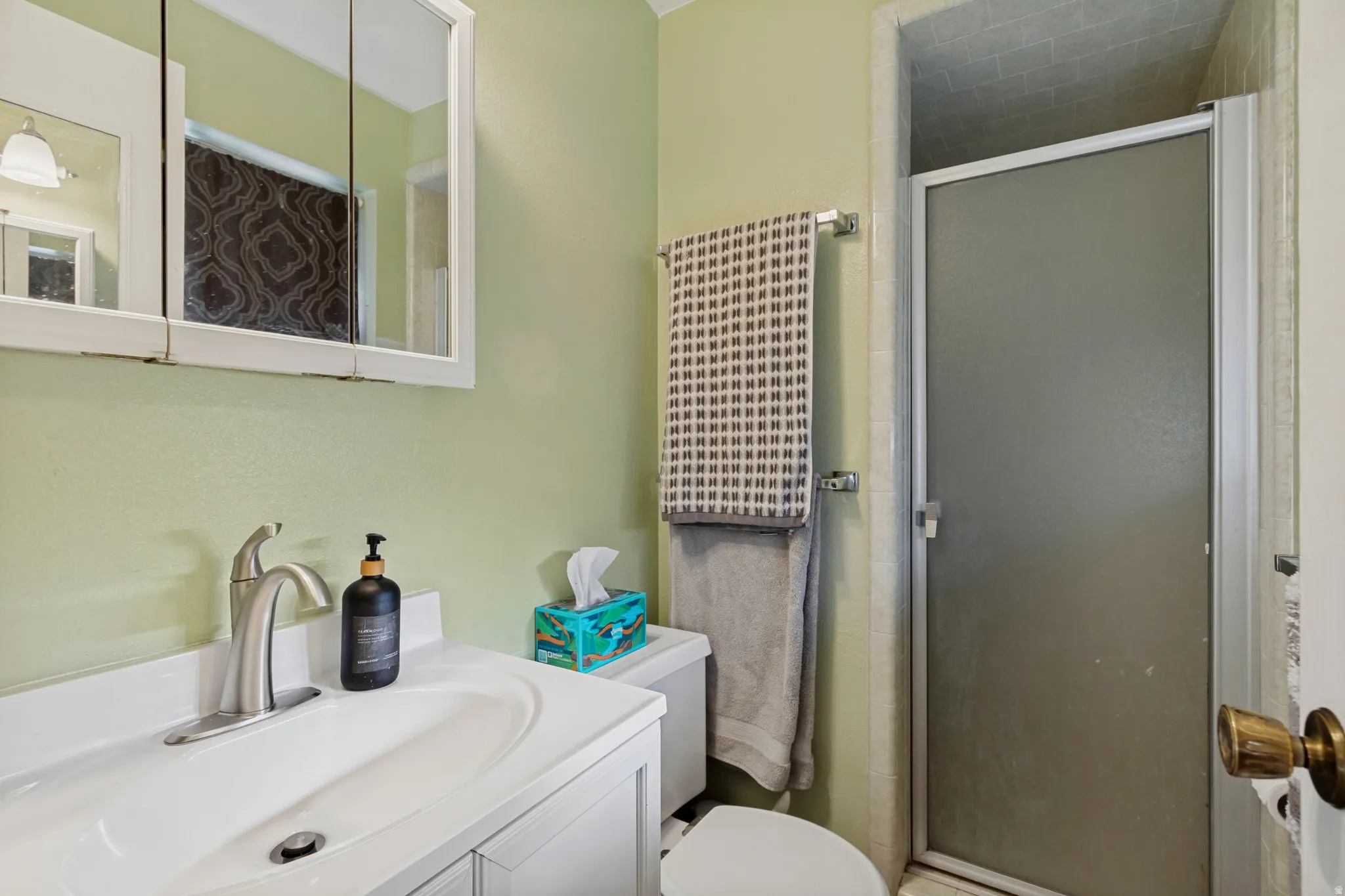 Bathroom featuring a white vanity with integrated sink, brushed nickel faucet, wall-mounted medicine cabinet, and a shower with a frosted glass door