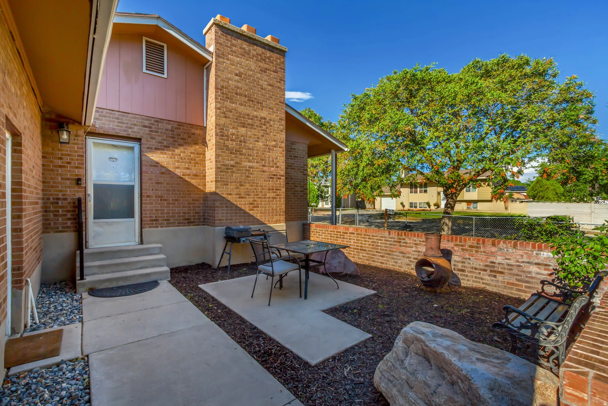 Brick exterior with a prominent brick chimney, concrete patio, concrete steps, and a low brick retaining wall