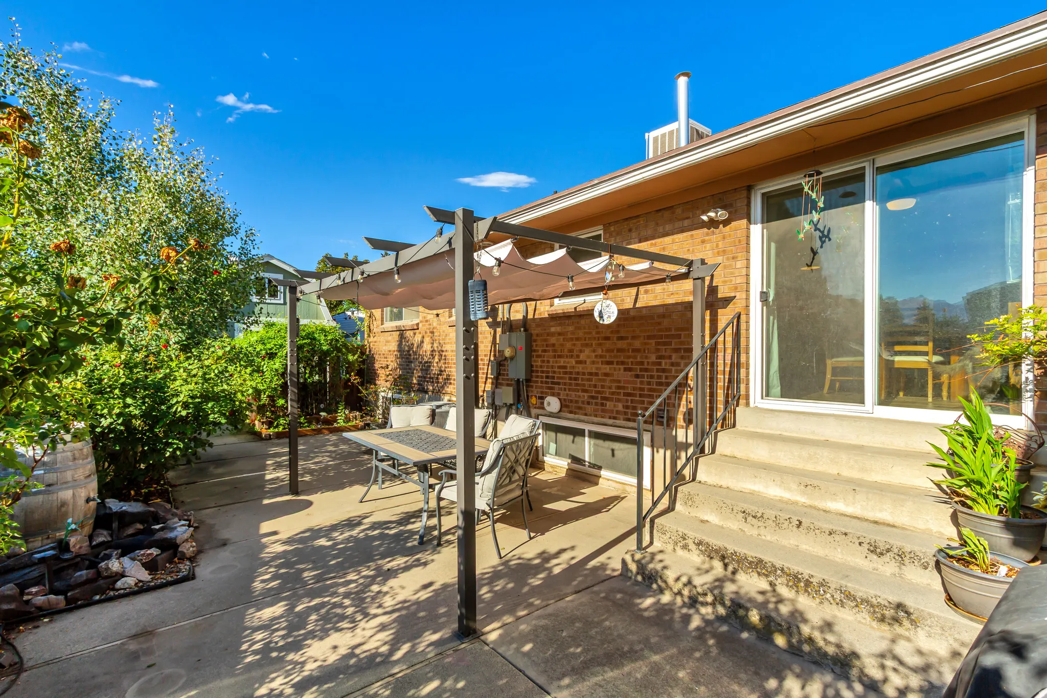 Brick exterior, concrete patio, sliding glass door, pergola with canopy, mature landscaping