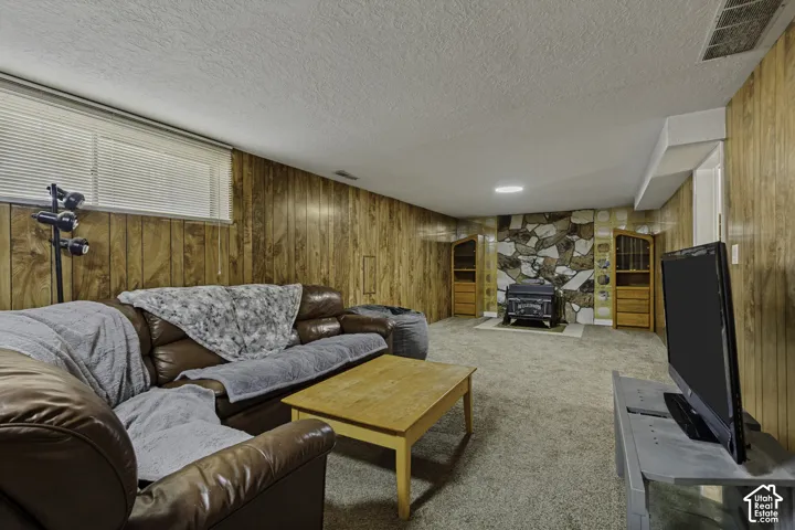 Wood paneling, stone accent wall, recessed lighting, carpet flooring, and a wood-burning stove