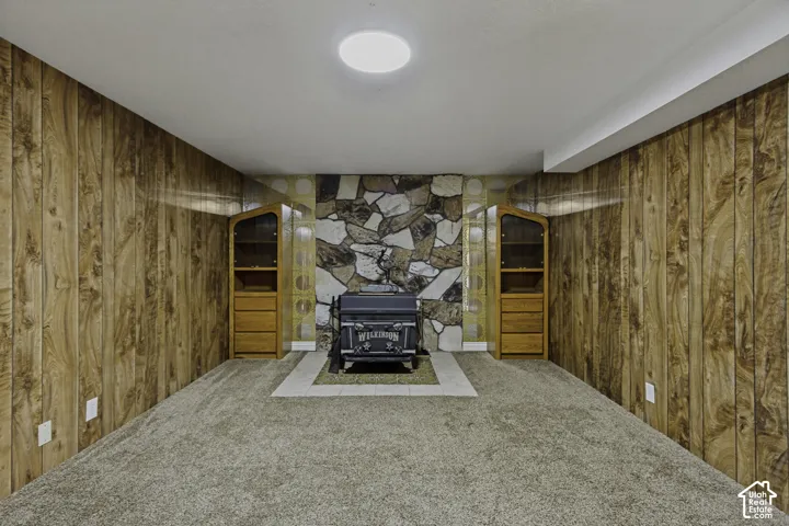 Wood paneling walls, stone-patterned accent wall, built-in display cabinetry, carpeted flooring, and a central ceiling light fixture