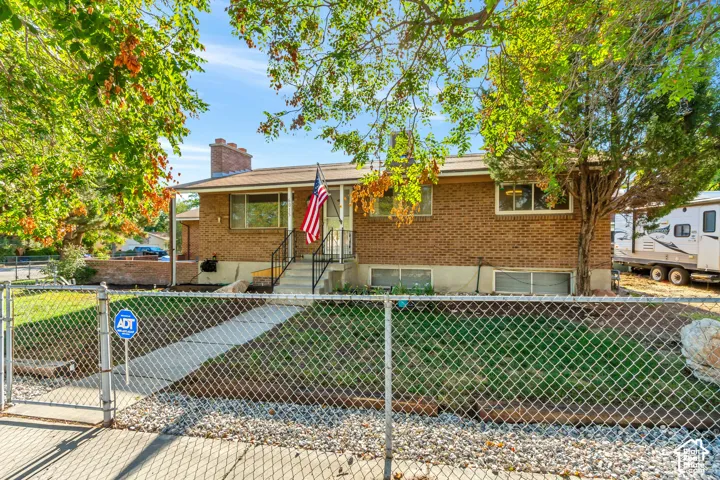 Brick exterior featuring a covered porch with railings, a concrete walkway, and a chain-link fence