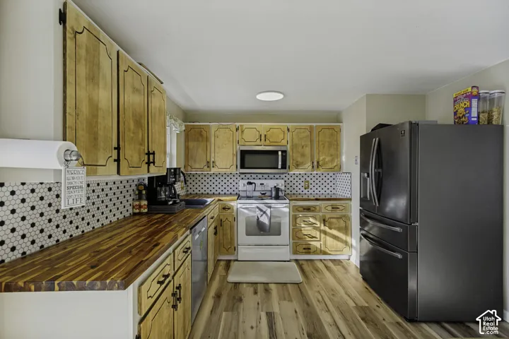 Wood-finish flooring, wood cabinetry with black hardware, hexagon tile backsplash, stainless steel appliances, and a built-in microwave