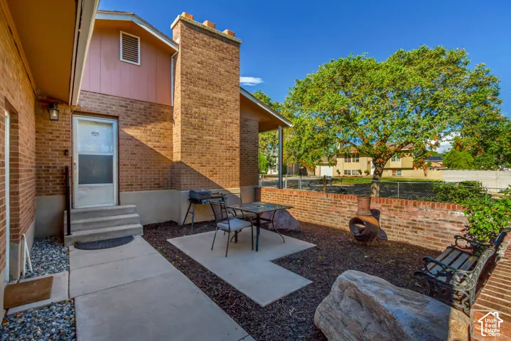 Brick exterior with a prominent brick chimney, concrete patio, concrete steps, and a low brick retaining wall