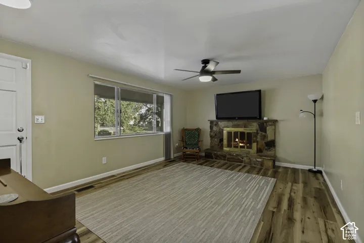 Wood-finish flooring, stone-clad fireplace with brass insert, ceiling fan with integrated lighting, and a front entry door with hardware