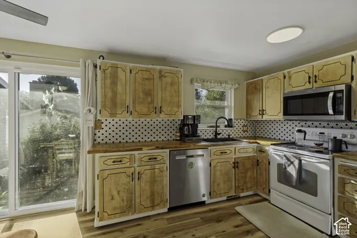 Kitchen featuring wood-finish flooring, wood cabinetry, white appliances, black and white geometric backsplash, and a sliding glass door
