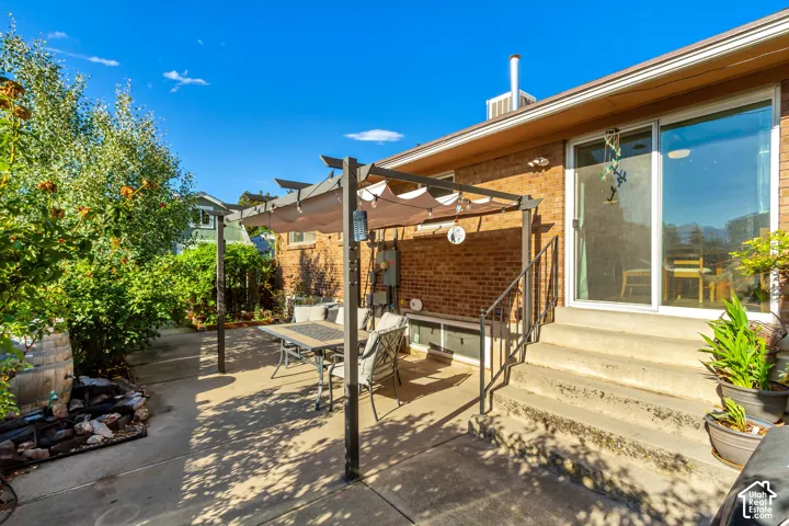 Brick exterior, concrete patio, sliding glass door, pergola with canopy, mature landscaping