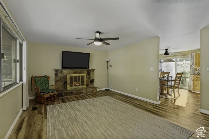 Living area featuring a stone-clad fireplace, wood-finish flooring, and a ceiling fan