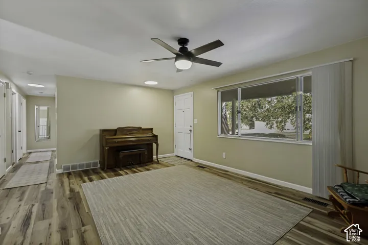 Wood-finish flooring, ceiling fan with integrated lighting, large window with vertical blinds, and neutral painted walls