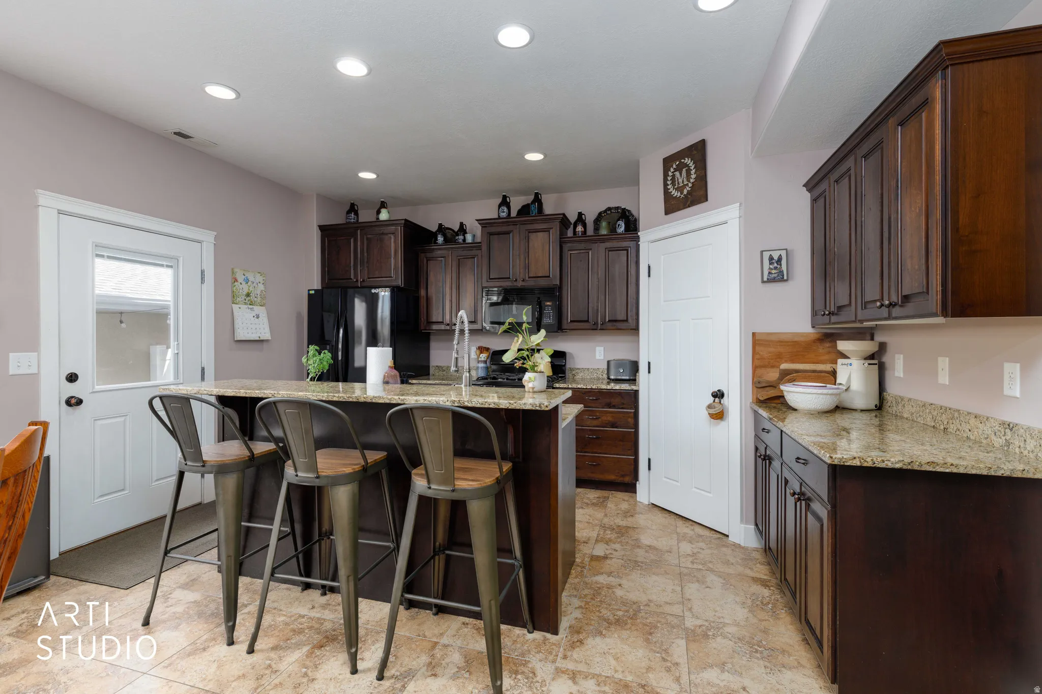 Kitchen featuring dark wood-finish cabinetry, light-toned countertops, a central island with bar seating, a built-in sink with a gooseneck faucet, and recessed lighting