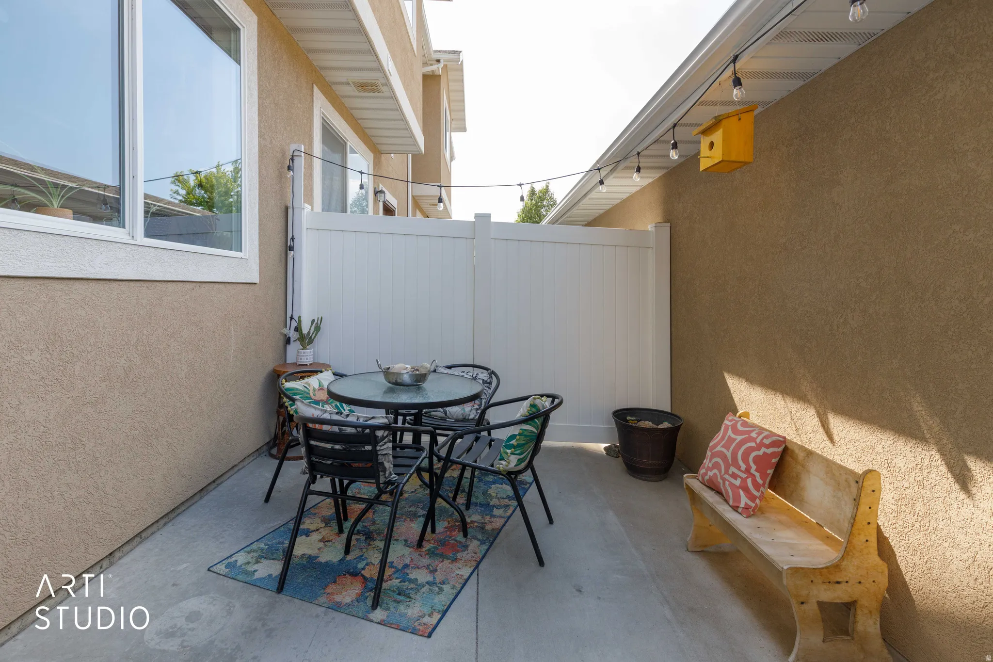 Private patio area featuring concrete flooring, a white privacy fence, and string lighting
