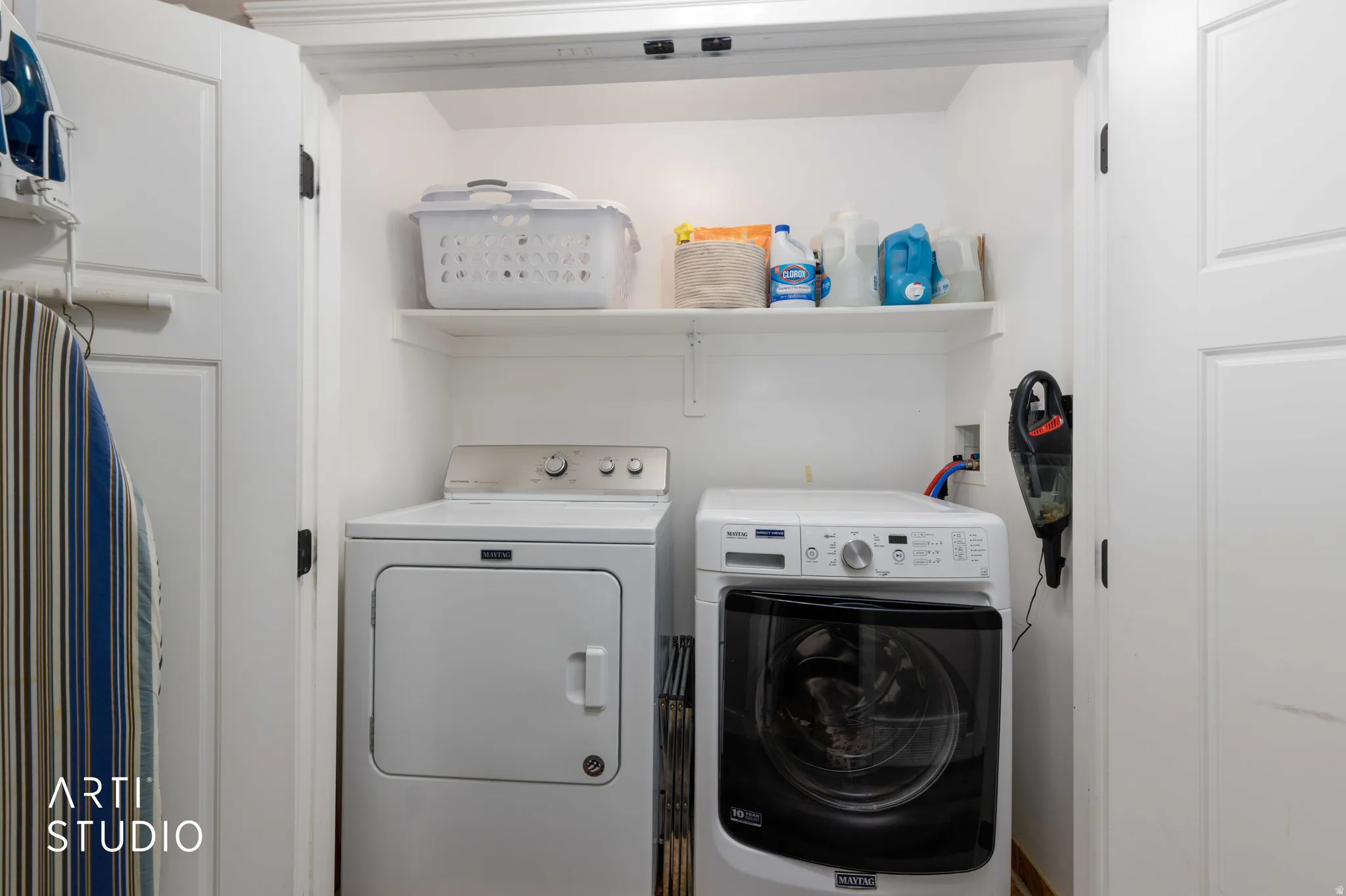 Integrated laundry closet with built-in shelving, white paneled doors, and a light-colored flooring