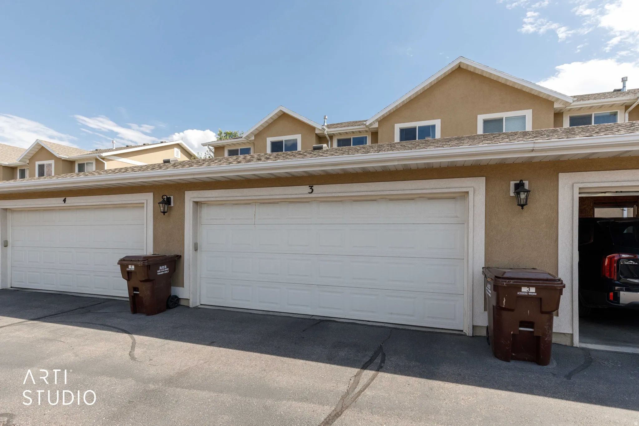 Exterior featuring multiple garage doors with carriage-style lighting fixtures, stucco siding, white trim, and upper-level windows