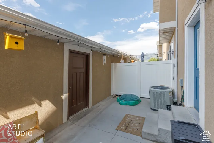 Enclosed concrete patio area featuring a privacy fence, exterior door, and an air conditioning unit
