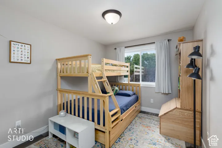 Bright, naturally lit bedroom featuring custom wood bunk bed with integrated storage, hardwood flooring, large picture window with white curtains, recessed ceiling lighting, and wood-finish wall-mounted shelving unit
