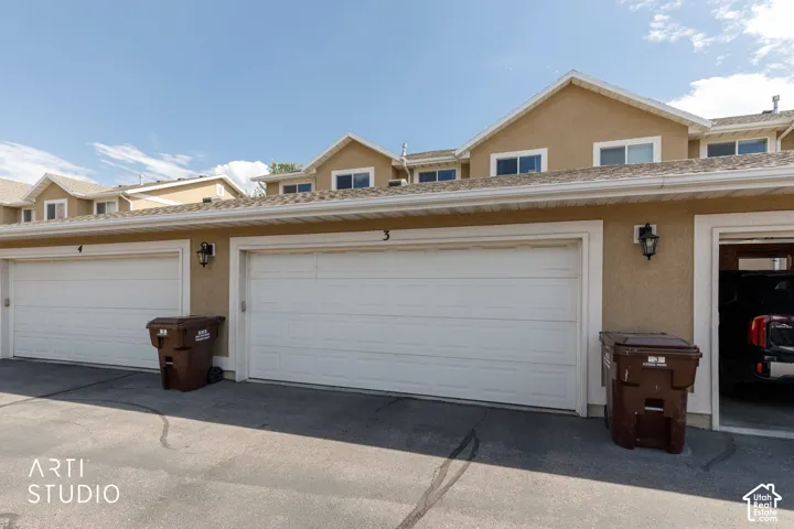 Exterior featuring multiple garage doors with carriage-style lighting fixtures, stucco siding, white trim, and upper-level windows