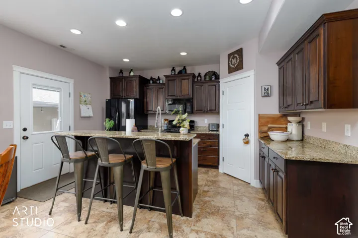 Kitchen featuring dark wood-finish cabinetry, light-toned countertops, a central island with bar seating, a built-in sink with a gooseneck faucet, and recessed lighting