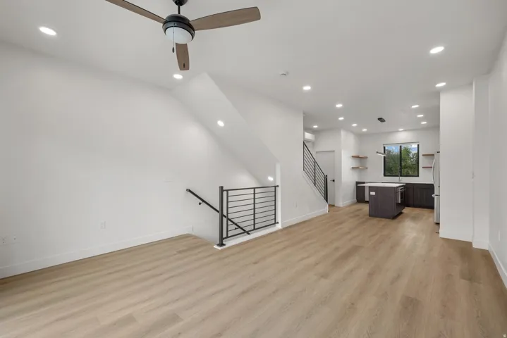 Open-concept living area with wood-finish flooring, recessed lighting, a modern ceiling fan, and a kitchen featuring dark cabinetry and a central island