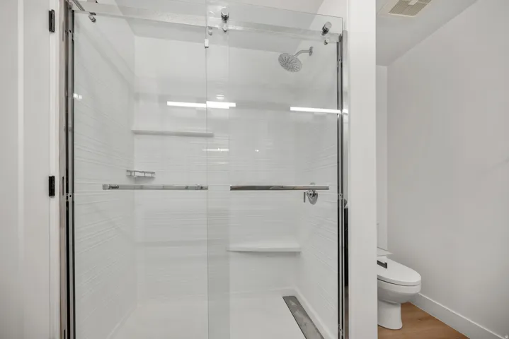Glass-enclosed shower with horizontal textured tile, integrated shelving, linear drain, and a wall-mounted showerhead
