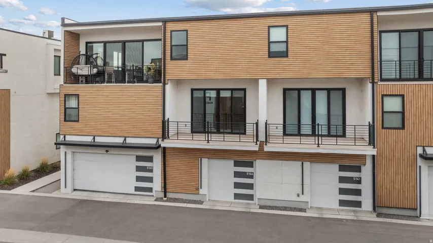 Modern townhome exterior featuring wood-finish siding, white stucco, multiple balconies with black railings, and attached garages with contemporary doors