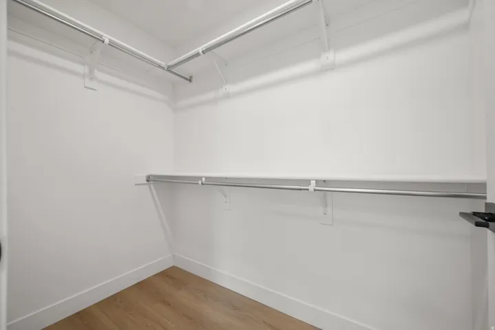 White painted walls with wood-finish flooring, featuring upper and lower metal hanging rods