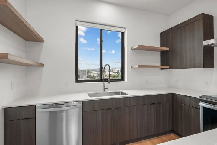 Contemporary kitchen featuring dark wood-finish cabinetry, light-toned countertops, a stainless steel sink with a gooseneck faucet, and stainless steel appliances