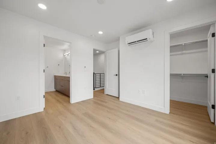 Primary Suite - White walls with recessed lighting, wood-finish flooring, and a wall-mounted air conditioning unit