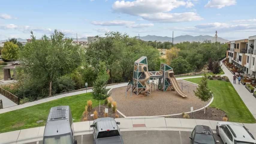 Community playground with multiple slides and climbing features, surrounded by green space, paved pathways, and mature trees