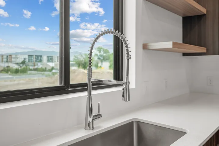 Stainless steel sink with a high-arch pull-down faucet, white solid surface countertops, and wood-finish open shelving